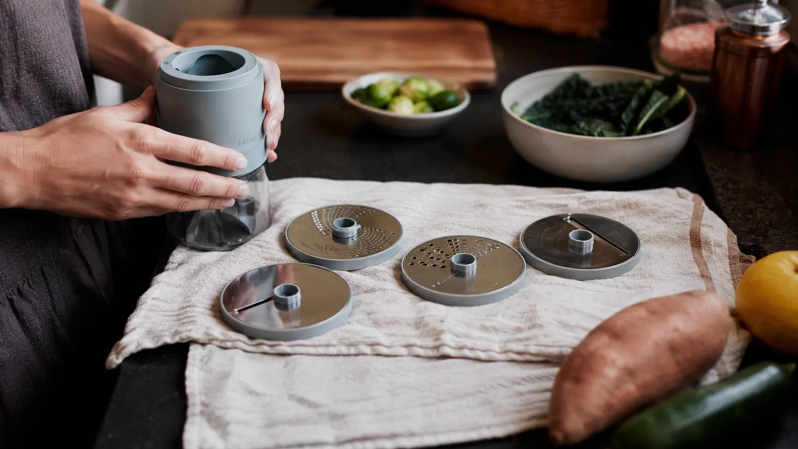 A spiralizer with interchangeable blade attachments laid out next to a small stack of kitchen drawer organizers