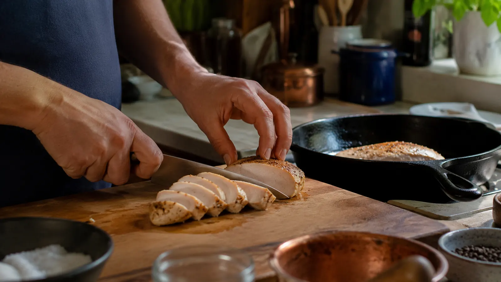 Sliced sous vide chicken breast on a cutting board next to a cast iron pan used for the final sear